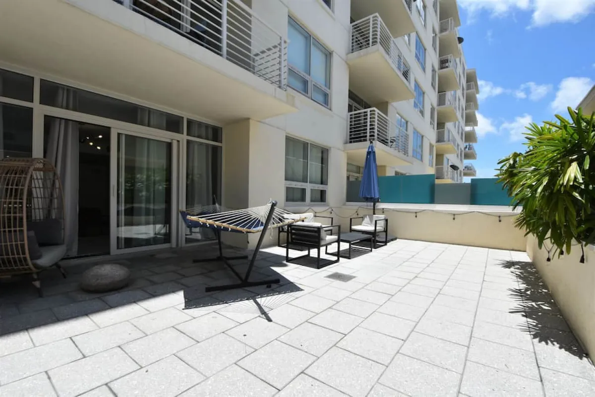 A spacious outdoor terrace with a freestanding hammock, outdoor seating area with chairs and a table under a large umbrella, and potted greenery along the wall. The terrace feels private yet open, inviting guests to enjoy Miami’s fresh air and sunshine.