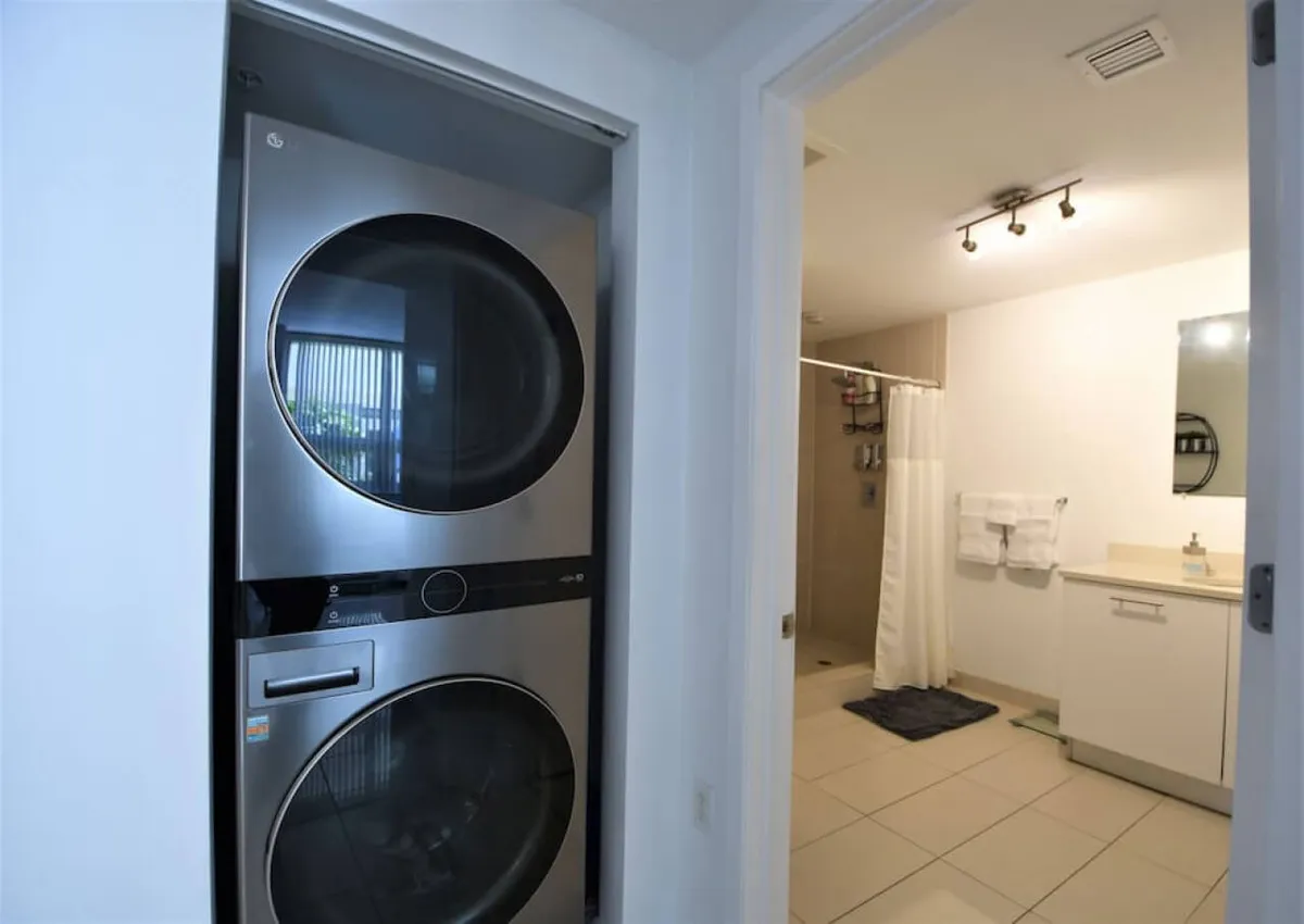 A view of a stacked washer and dryer unit conveniently placed beside a bathroom with a shower and vanity. The area is compact yet efficient, underlining the practicality of in-unit amenities.